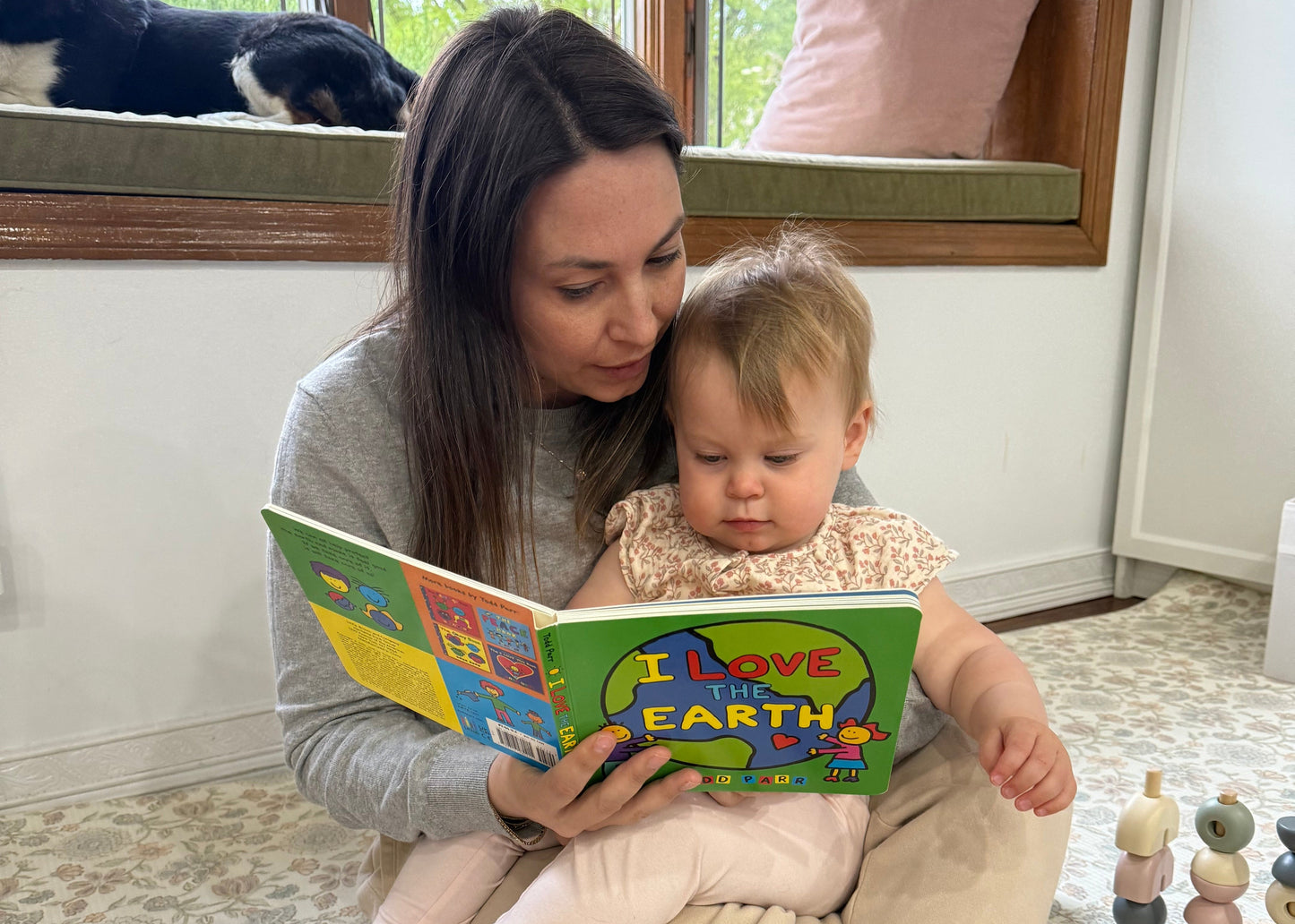 A child being tutored by an adult educator while sitting on the floor, with a colorful book being read to the child.
